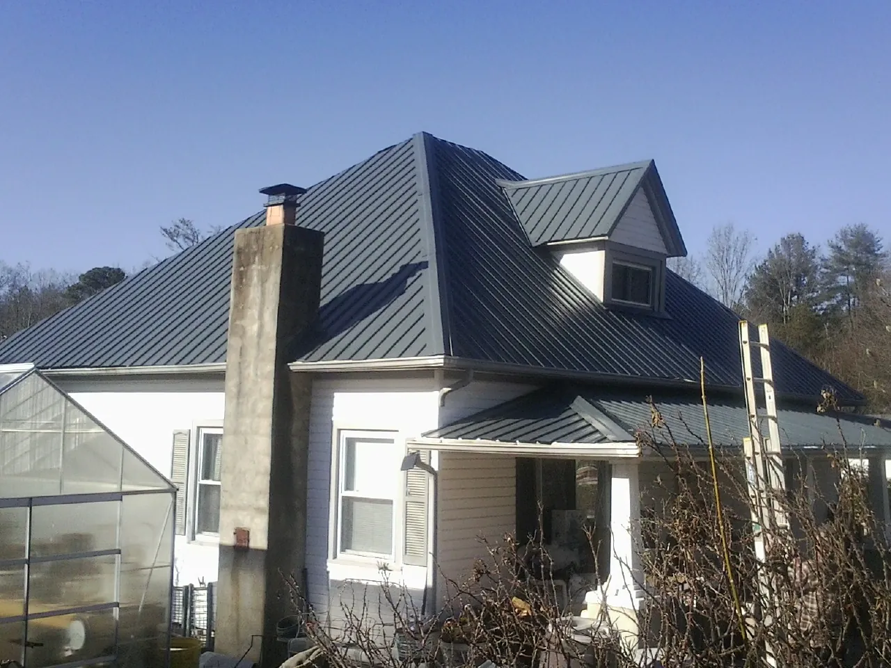 Dark blue standing seam metal roof on a white farmhouse with dormer — Slate & Tile Roof Repair by Roofing Brothers in Foster